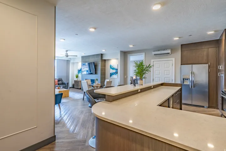 Modern kitchen featuring dual waterfall-edge quartz countertops, wood-finish cabinetry, stainless steel refrigerator, recessed ceiling lighting, and an open layout connecting to the living area with wood-finish flooring throughout