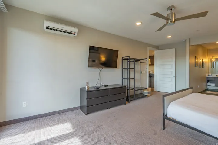 Spacious primary bedroom suite featuring neutral carpeting, ceiling fan with integrated lighting, wall-mounted flat-screen television, and direct access to an ensuite bathroom