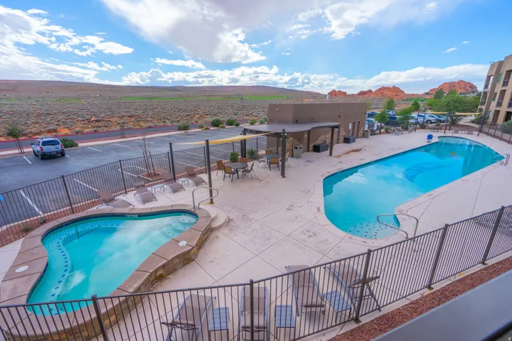 Resort-style outdoor living featuring two lagoon-shaped swimming pools with curved edges, surrounding travertine decking, and black metal safety fencing