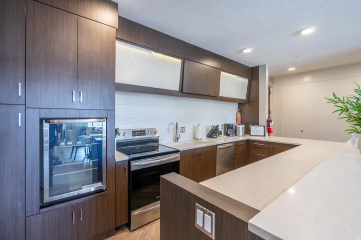 Modern kitchen featuring dark wood-finish cabinetry, stainless steel appliances, a built-in beverage cooler, light-toned countertops, and recessed lighting