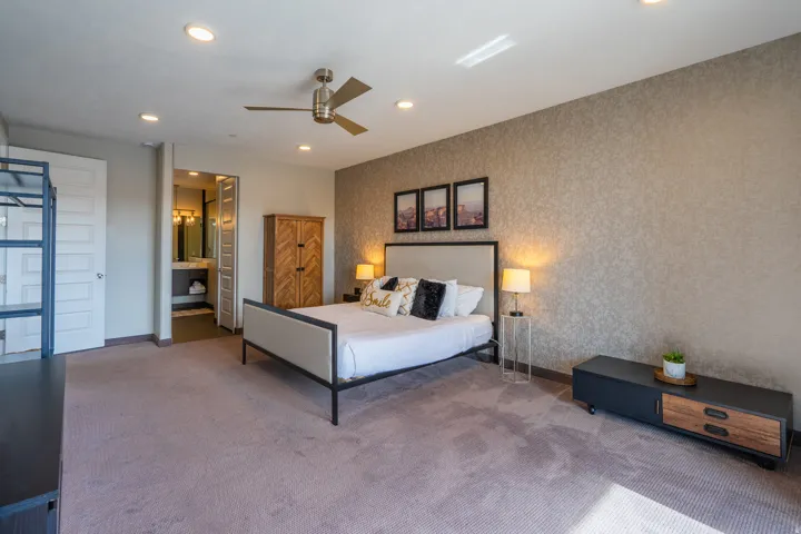 Recessed lighting, ceiling fan, textured accent wall, light-toned carpet, and an en-suite bathroom with a dual vanity
