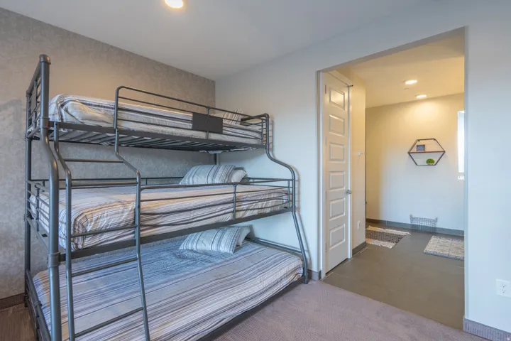 Triple bunk bed with metal frame, textured accent wall, recessed lighting, and carpeted flooring