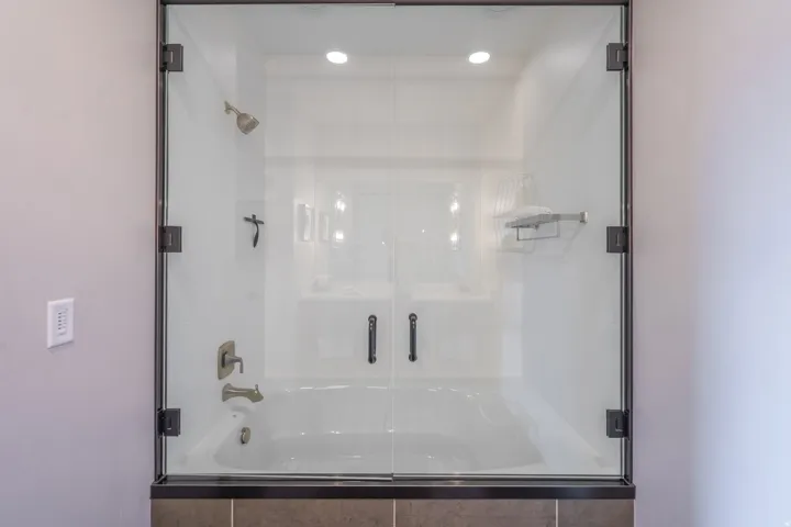 Bathtub and shower combination with clear glass enclosure and dark bronze hardware