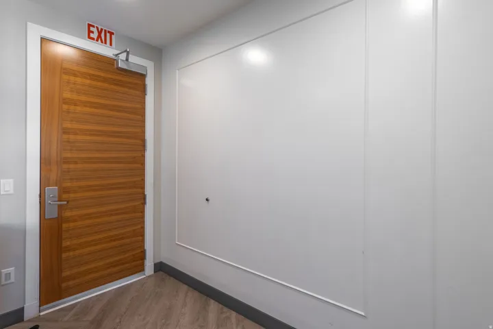 Wood-finish door with brushed metal hardware, light gray walls, white decorative wall paneling, and wood-finish flooring