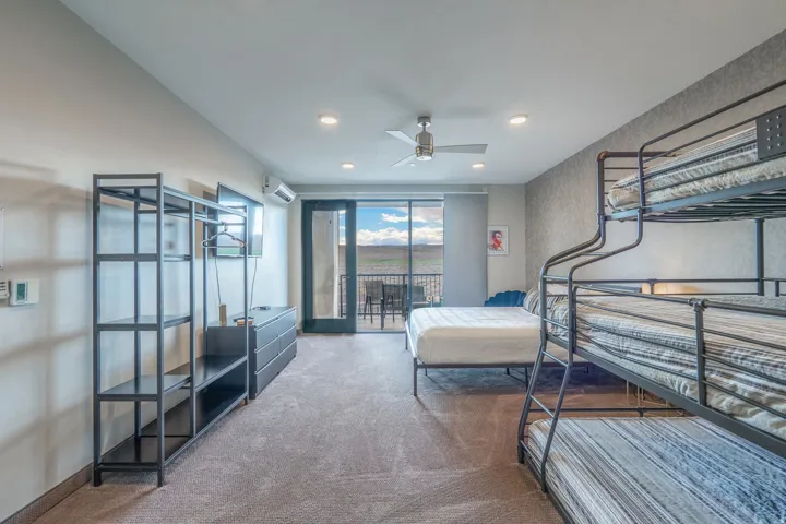 Modern dormitory-style bedroom featuring multiple bunk beds with striped bedding, polished concrete flooring, and abundant natural light from expansive glass doors opening to a balcony
