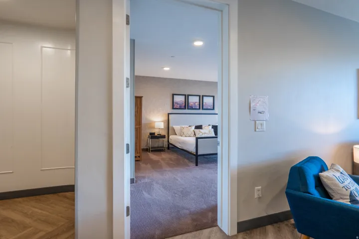 Bright hallway with clean sightlines opening to a spacious bedroom featuring wood-finish flooring, recessed ceiling lighting, and neutral wall finishes