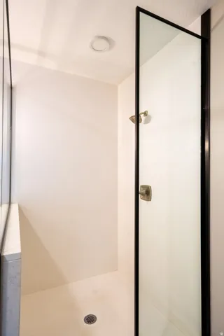 Modern shower enclosure featuring a frameless glass panel with matte black hardware, a linear floor drain, and clean white tile surround with recessed ceiling lighting
