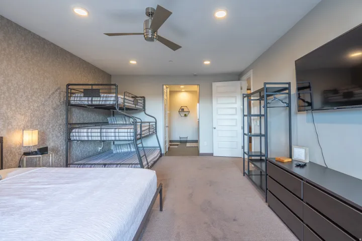 Spacious bedroom suite featuring multiple sleeping areas with metal bunk bed frames, carpet flooring, recessed ceiling lighting, ceiling fan, and direct access to an ensuite bathroom