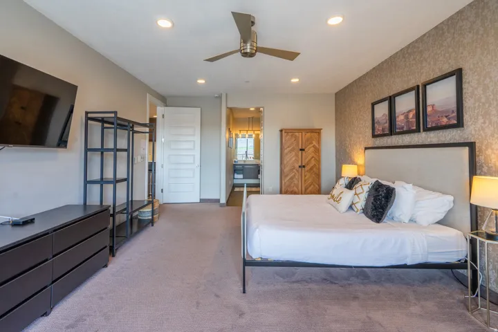 Recessed lighting, ceiling fan, textured accent wall, and an open doorway leading to an additional space