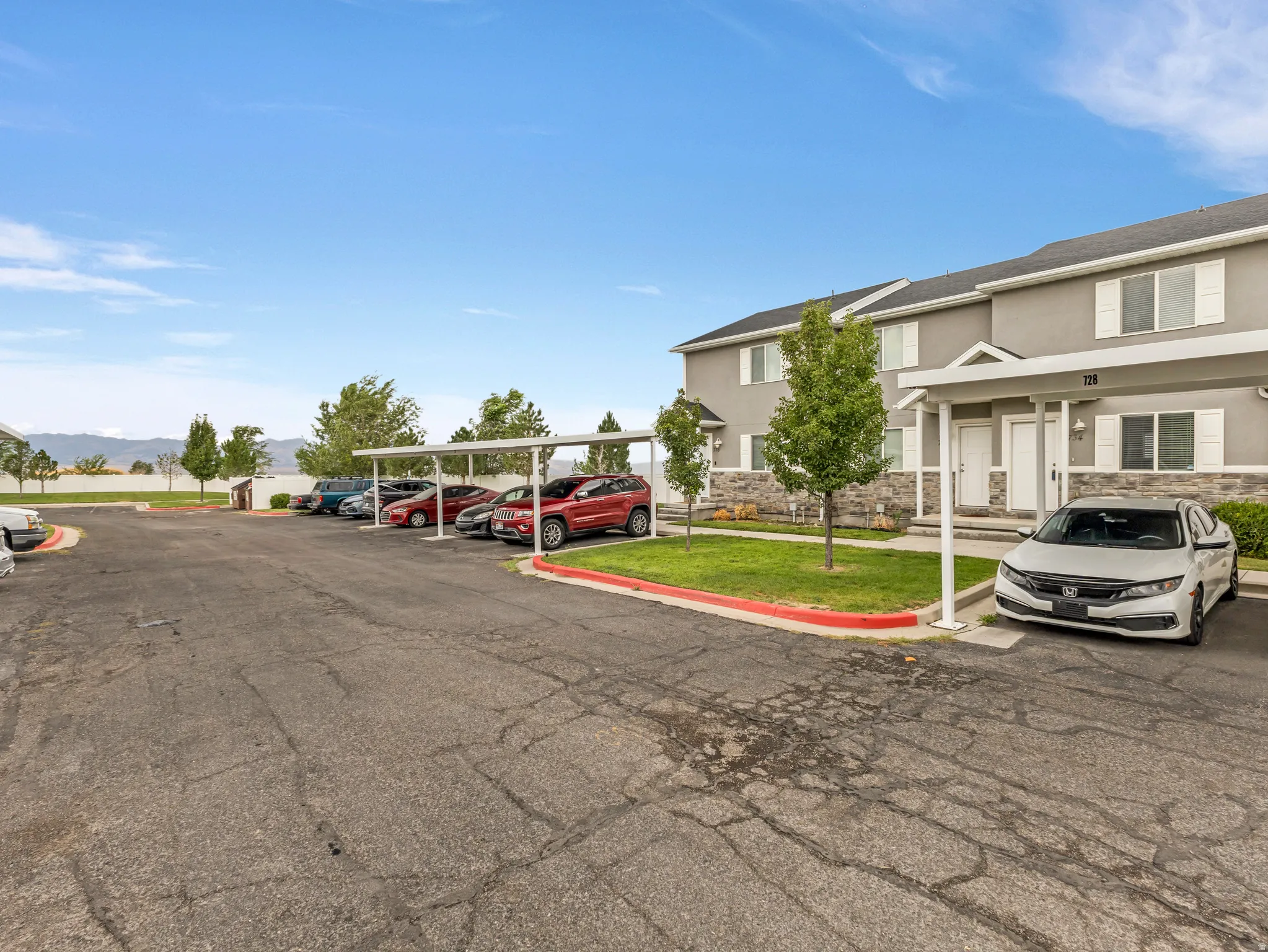 Spacious parking area with dedicated spaces and professional landscaping featuring mature trees, manicured lawn, and vibrant red accent borders