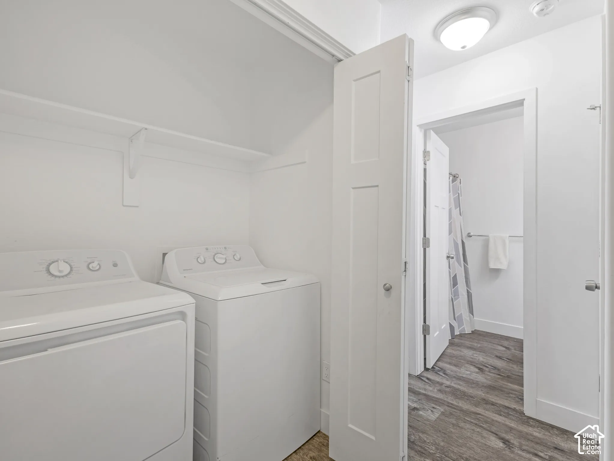 Dedicated laundry area with shelving, accompanied by wood-finish flooring extending into an adjacent space