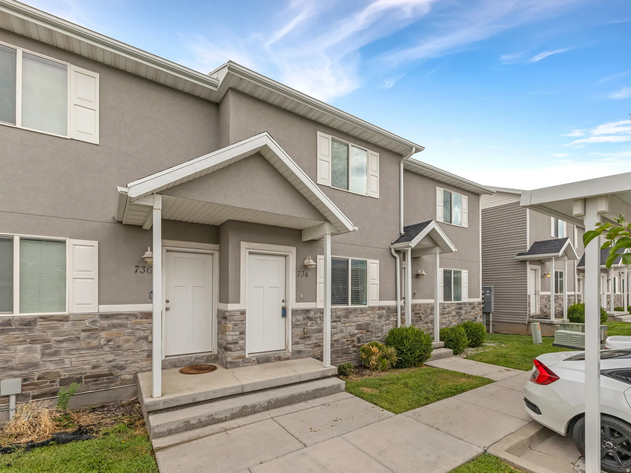 Modern townhome featuring a welcoming front entrance with a covered porch, stone and stucco exterior detailing, white trim accents, and manicured landscaping
