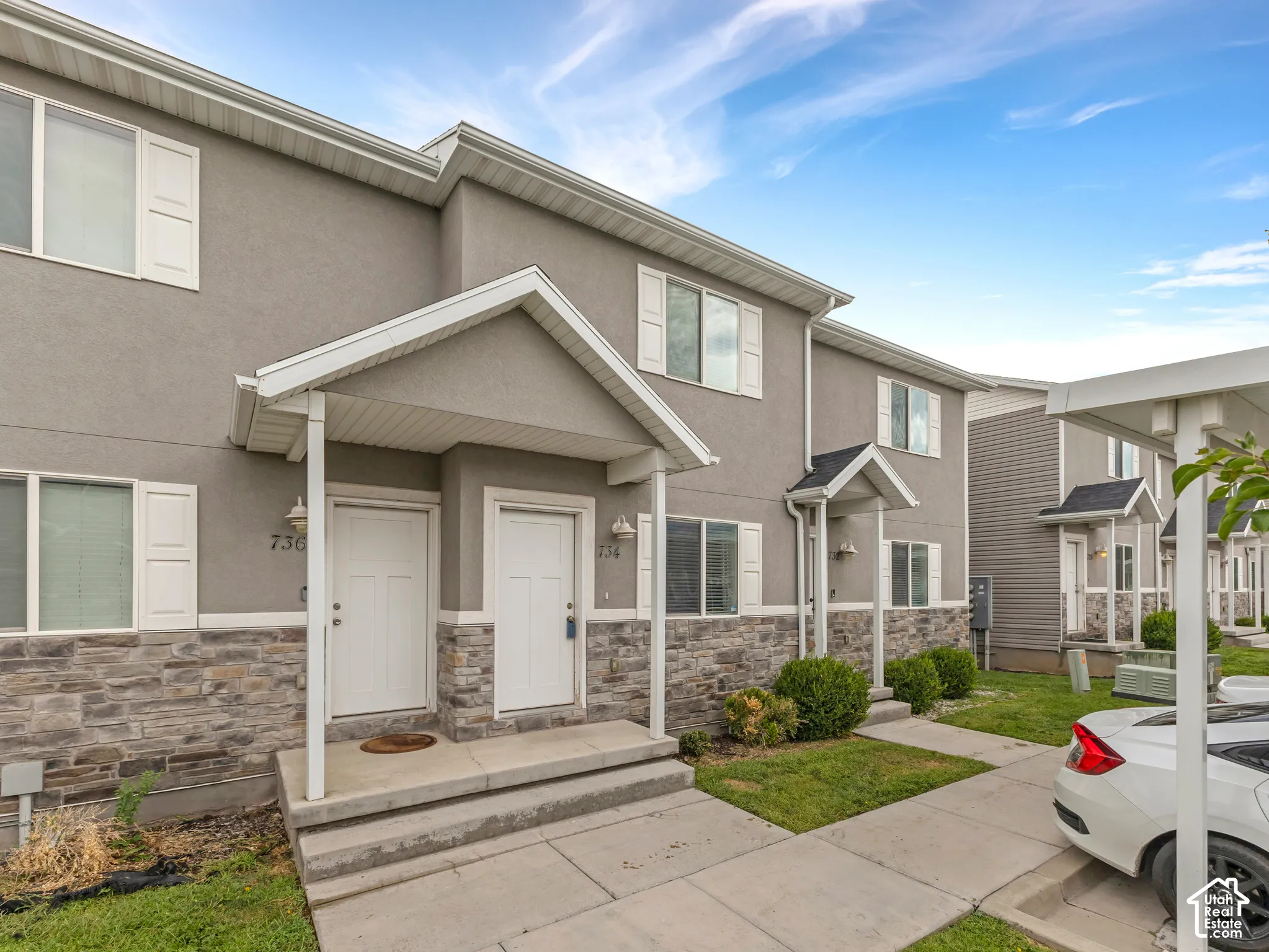 Modern townhome featuring a welcoming front entrance with a covered porch, stone and stucco exterior detailing, white trim accents, and manicured landscaping