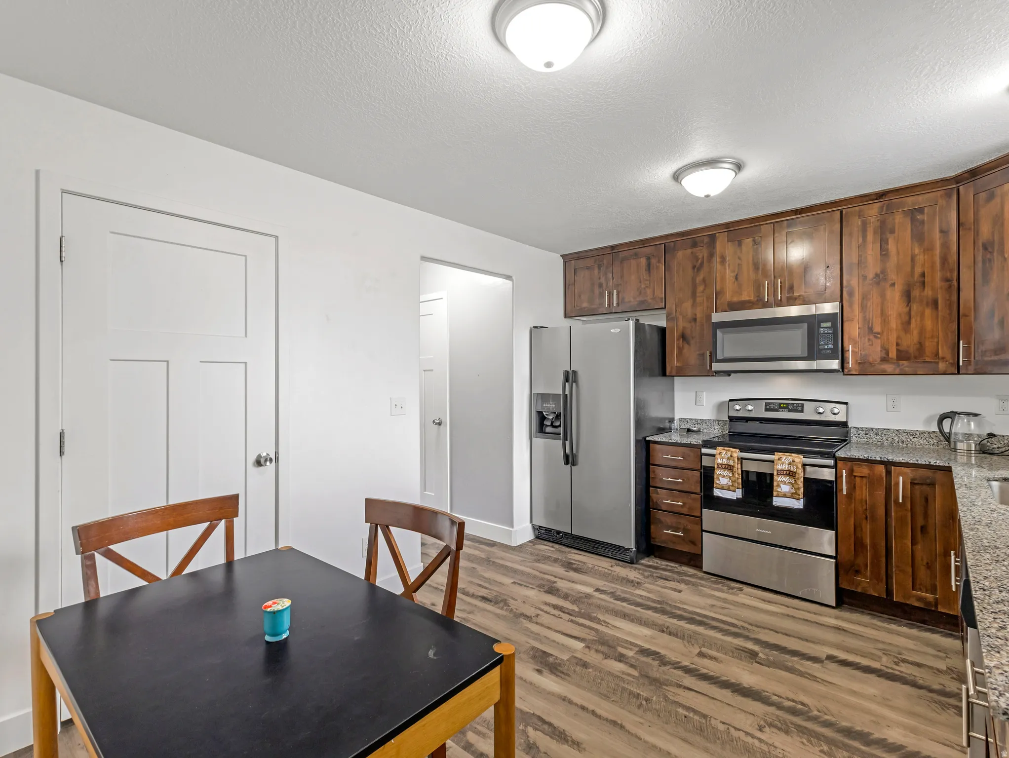 Spacious kitchen featuring warm wood cabinetry, stainless steel appliances including a gas range and side-by-side refrigerator, wood-finish flooring, and a dining area with seating for four
