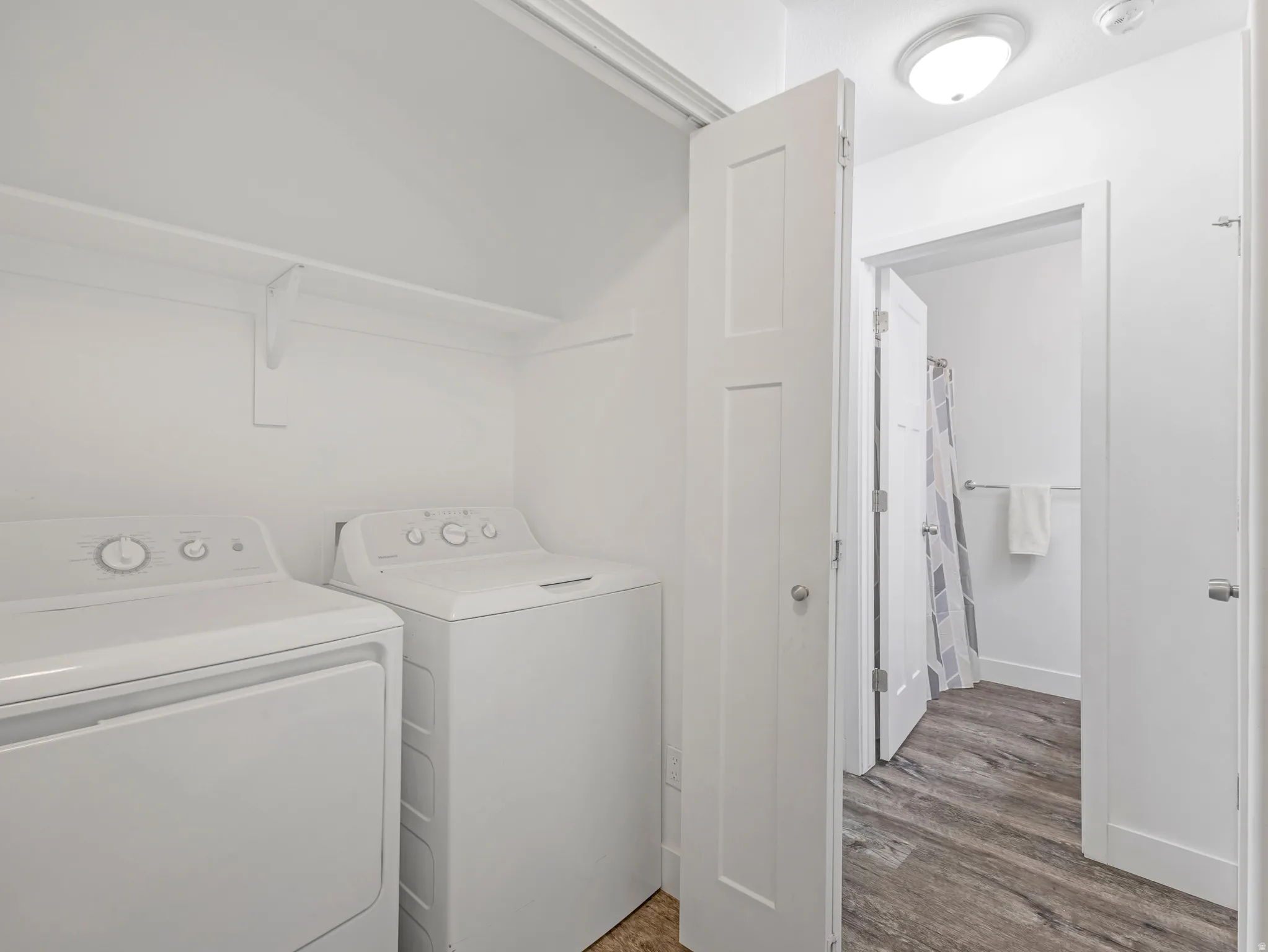 Dedicated laundry area with shelving, accompanied by wood-finish flooring extending into an adjacent space