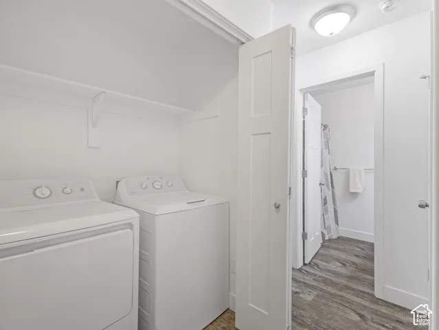Dedicated laundry area with shelving, accompanied by wood-finish flooring extending into an adjacent space