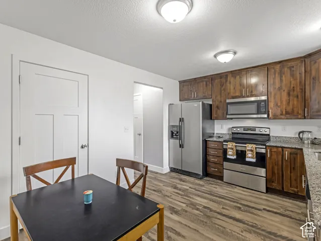 Spacious kitchen featuring warm wood cabinetry, stainless steel appliances including a gas range and side-by-side refrigerator, wood-finish flooring, and a dining area with seating for four