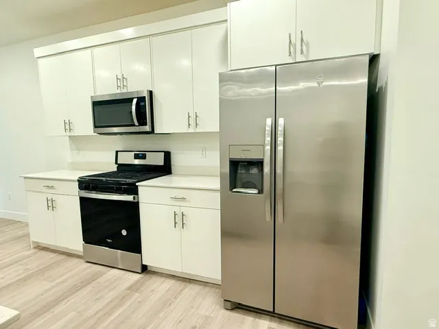 Kitchen featuring white cabinetry, light-toned countertops, wood-finish flooring, and stainless steel appliances
