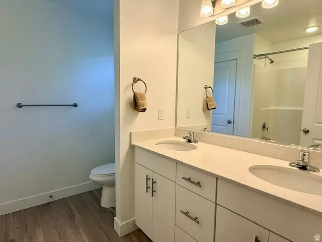 Dual vanity with light-toned countertops, chrome fixtures, integrated sinks, white cabinetry, and wood-finish flooring