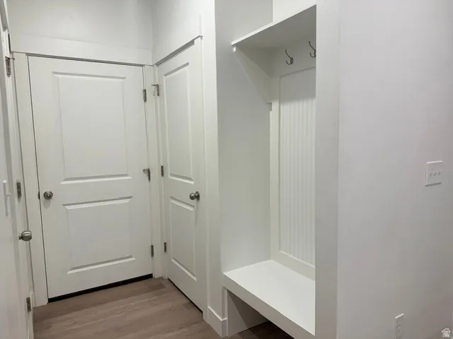 Entryway featuring white doors, wood-finish flooring, and a built-in bench with coat hooks