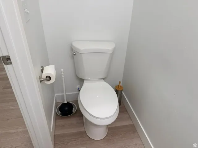 White toilet with a round bowl, light gray wood-finish flooring, and white wall trim
