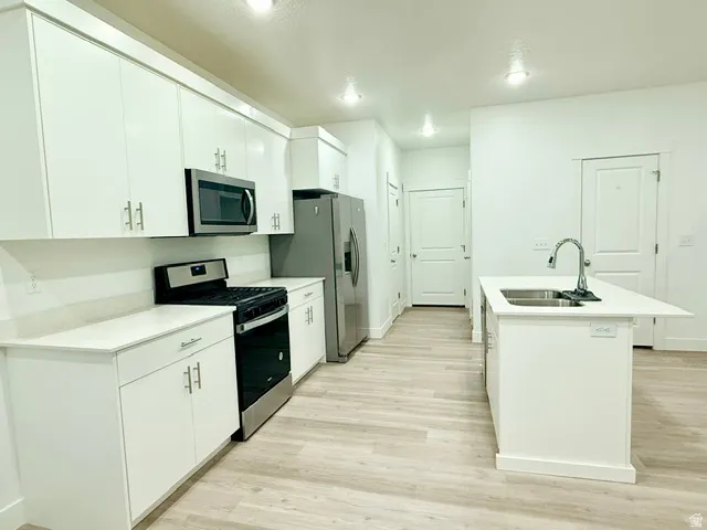 Modern kitchen featuring white cabinetry, stainless steel appliances, a center island with sink, light wood-finish flooring, and recessed lighting