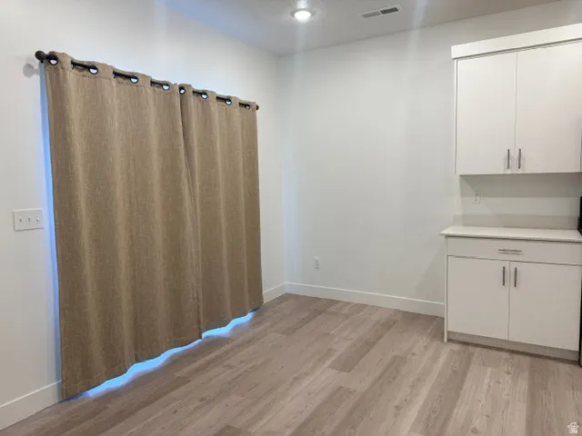 Modern utility space featuring wood-finish plank flooring, grommet-top window treatments with accent lighting, and white cabinetry with brushed metal hardware