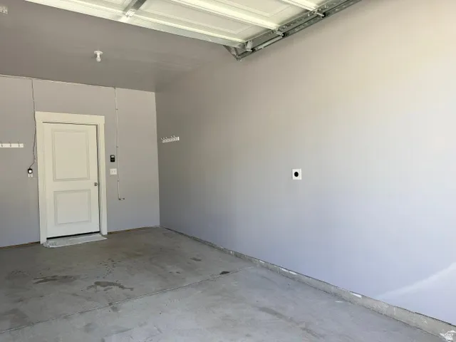 Attached garage space with a white paneled door, light gray painted walls, and a concrete floor