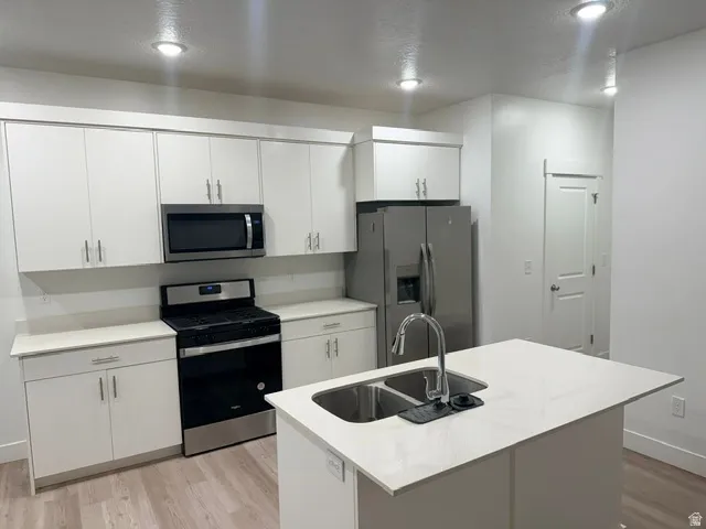 Kitchen featuring white cabinetry, stainless steel appliances, a center island with an undermount sink, recessed lighting, and wood-finish flooring