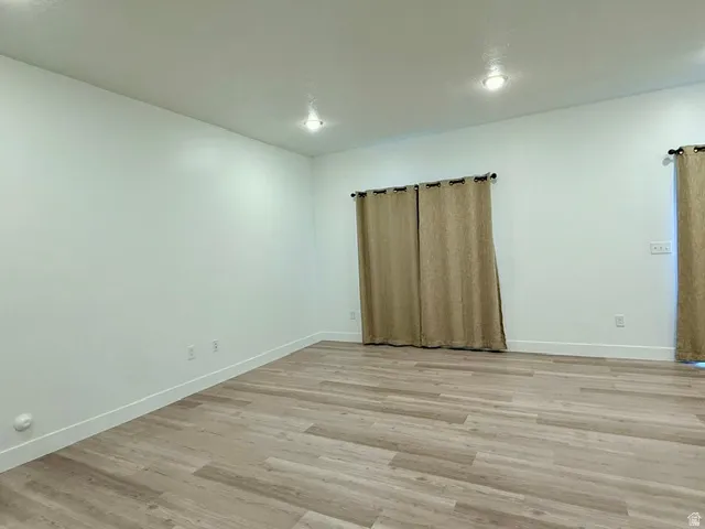 Spacious room featuring newly installed wood-finish flooring, recessed ceiling lighting, and large windows dressed with neutral curtain panels