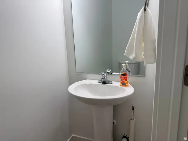 Pedestal sink with chrome faucet, mirror, and white walls