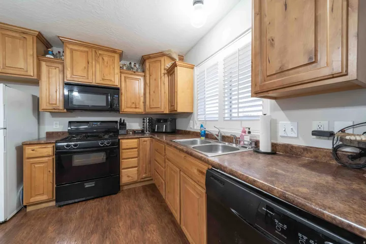 Kitchen featuring wood-finish cabinetry, black appliances, a double basin sink, and a window with blinds