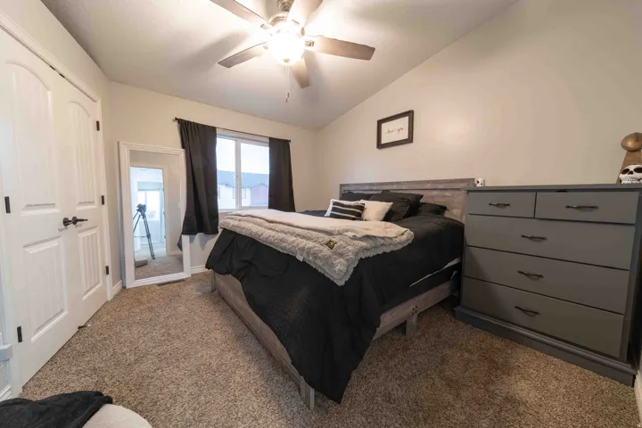 Vaulted ceiling with a ceiling fan, carpeted flooring, and a window with dark curtains