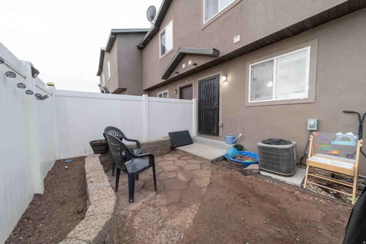 Private outdoor patio with a stone-finish retaining wall, paver stone hardscaping, and white vinyl fencing
