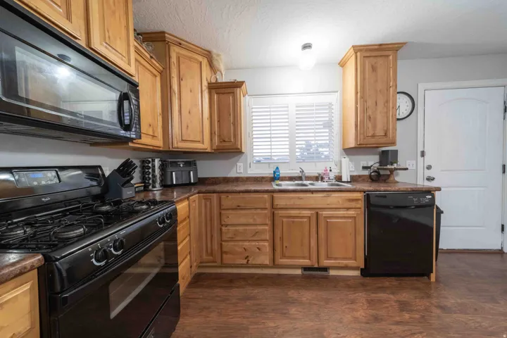 Wood-finish flooring, wood cabinetry, black appliances including a range and microwave, and a double-basin sink