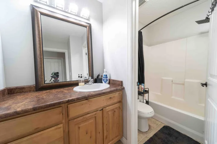 Spa-inspired bathroom featuring a wood-finish vanity with dual-sink capacity, rich wood-tone cabinetry with ample storage, a framed mirror with integrated lighting, and a tile-enclosed shower-tub combination