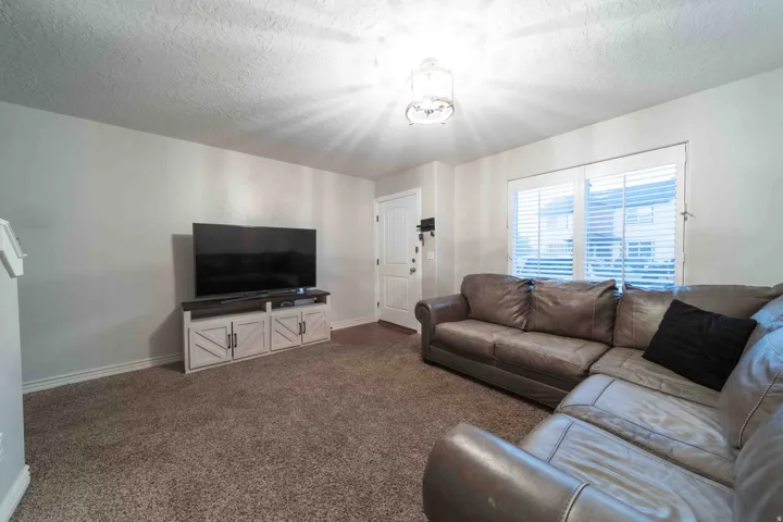 Spacious living room featuring neutral carpeting, a media console with storage, large windows with plantation shutters providing natural light, and recessed ceiling lighting throughout the open layout