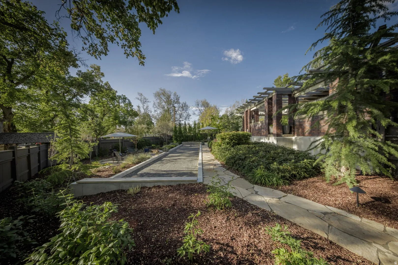 Expansive outdoor space featuring a bocce ball court, flagstone pathway, mature trees, and landscaping