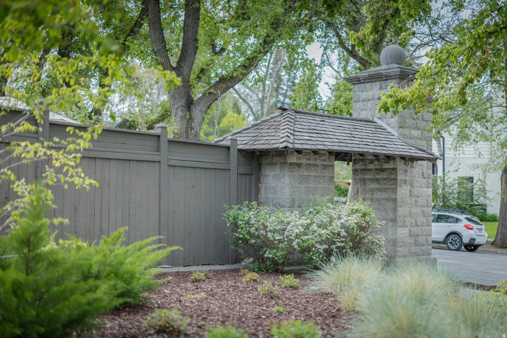Stone entryway with a wood shingle roof, complemented by a painted privacy fence and established trees