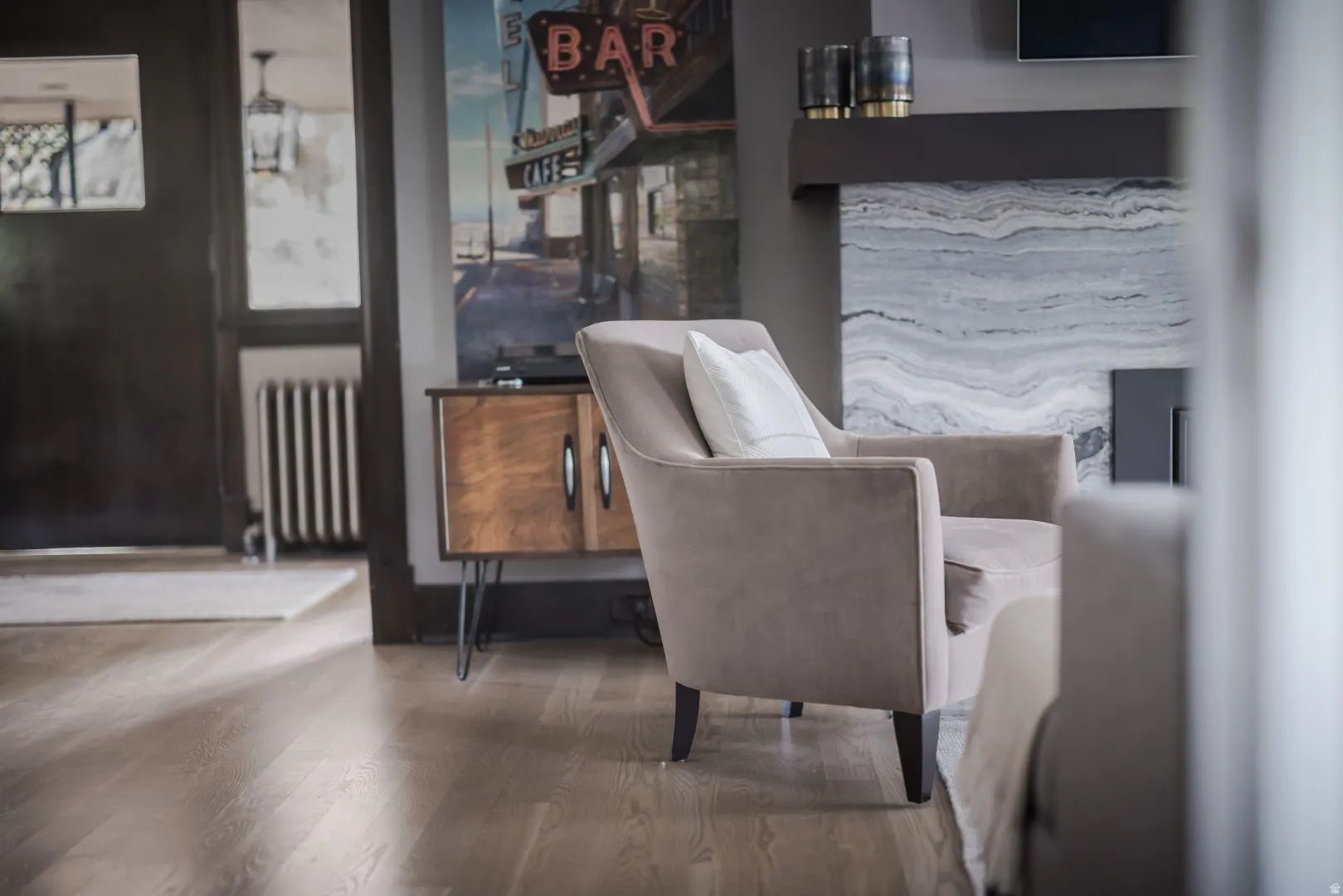 Wood-finish flooring, dark wood door frame, built-in radiator, and a fireplace with a stone surround