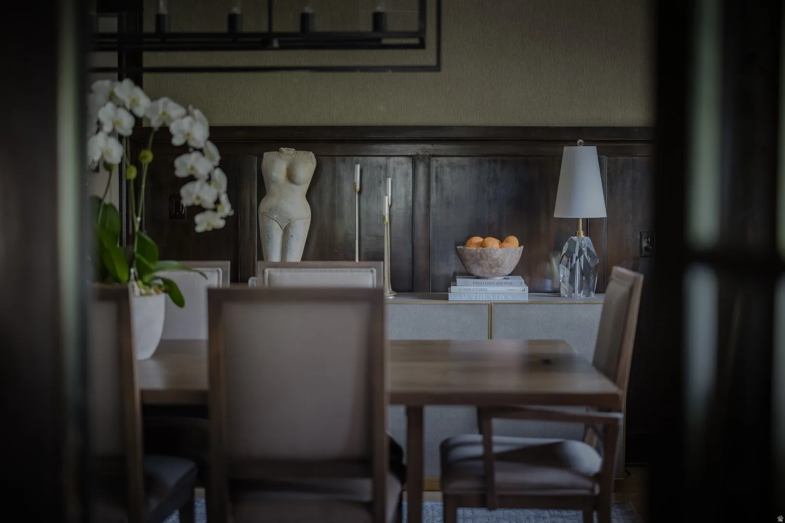 Elegant dining space showcasing neutral upholstered chairs, wood-finish table, and dark wood cabinetry with glass fronts