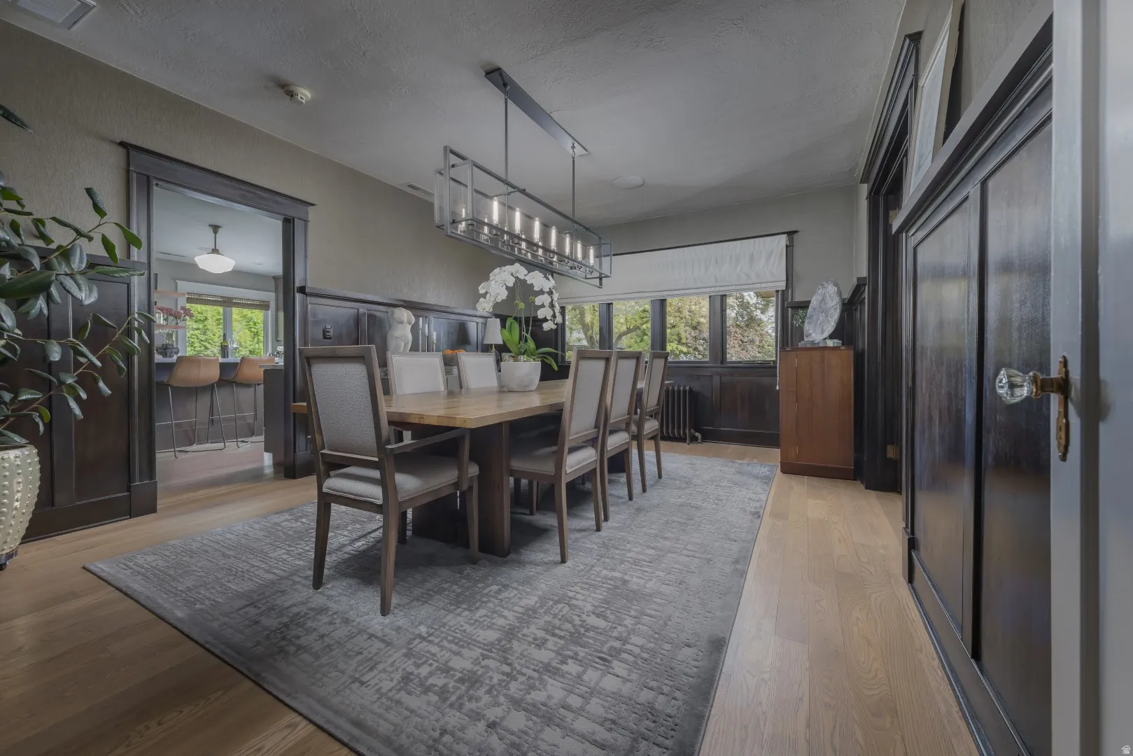 Wood-finish flooring throughout, featuring a linear chandelier and dark wood paneling
