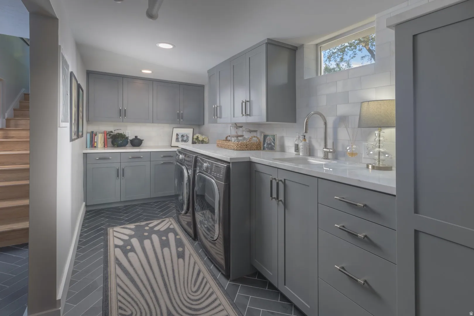 Herringbone pattern tile flooring, extensive gray cabinetry with modern hardware, white countertops, subway tile backsplash, and a built-in sink with a gooseneck faucet
