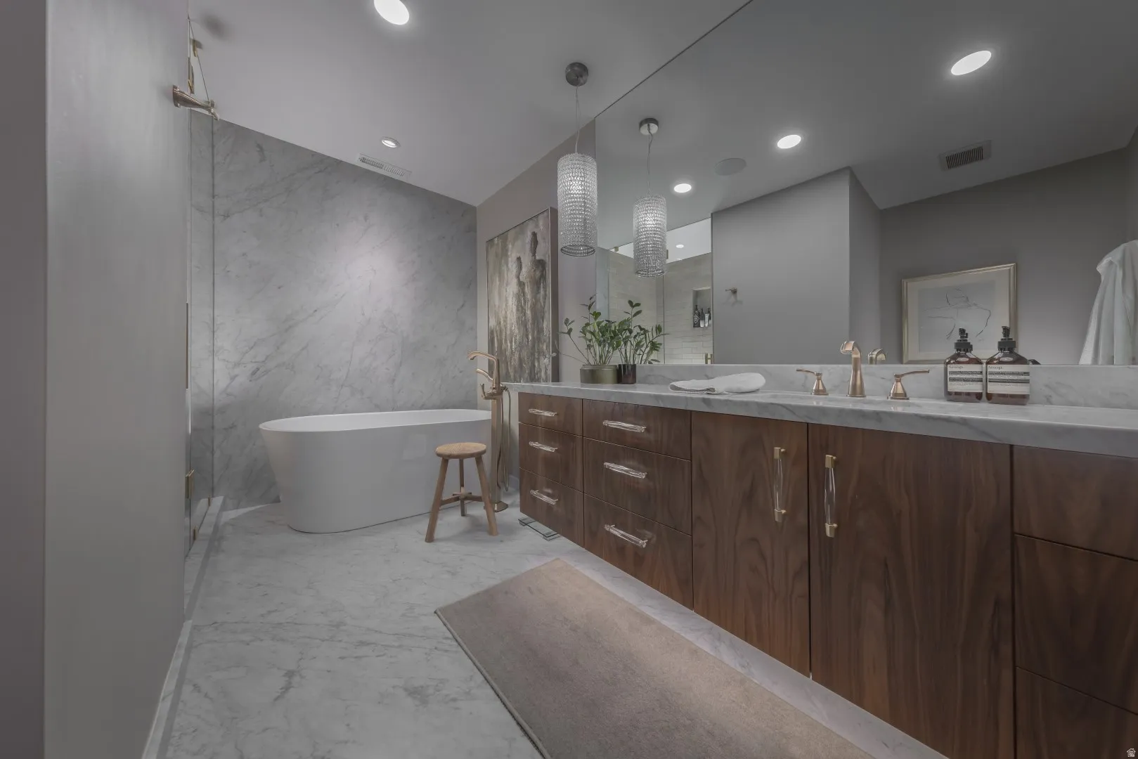 Primary Bathroom. Freestanding soaking tub, large-format marble-look wall tiles, marble-look flooring, double vanity with wood-finish cabinetry, and double pendant lighting