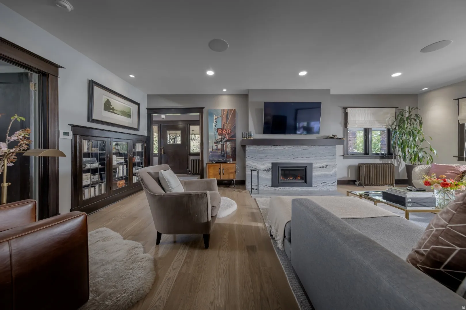 Light wood-finish flooring, built-in fireplace with a stone surround, built-in dark wood cabinetry, recessed lighting, and dark wood trim