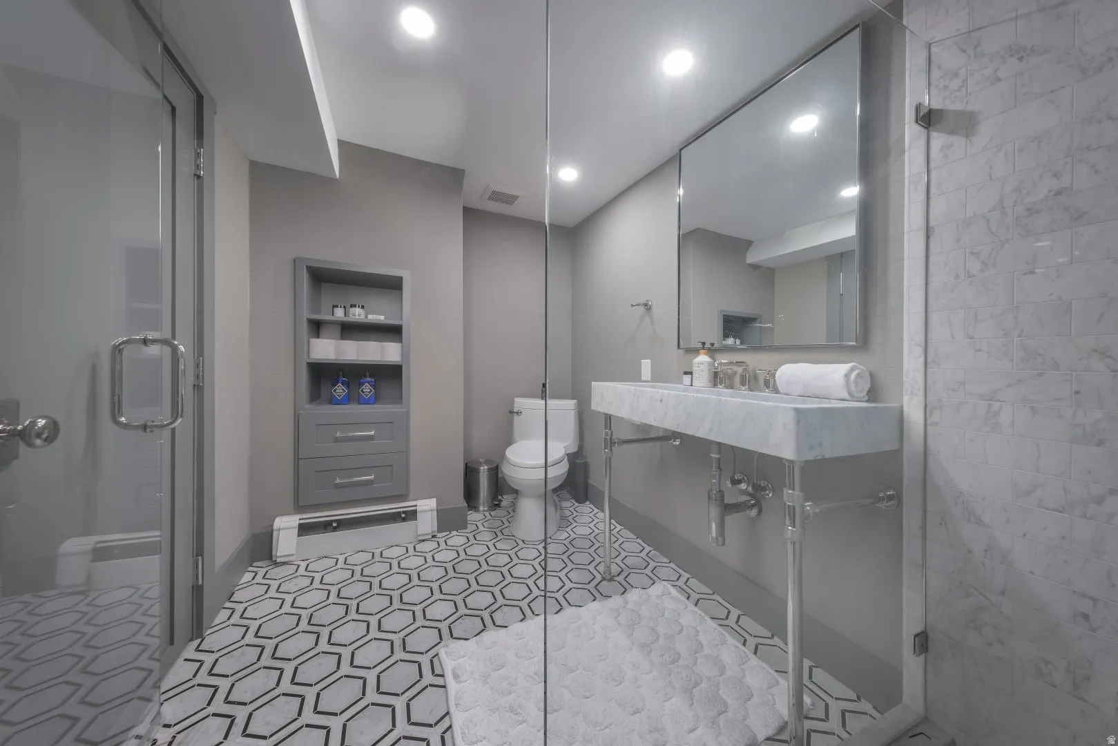 Hexagonal tile flooring, full-height marble shower surround, wall-mounted vanity with integrated sink, rectangular mirror, and recessed lighting