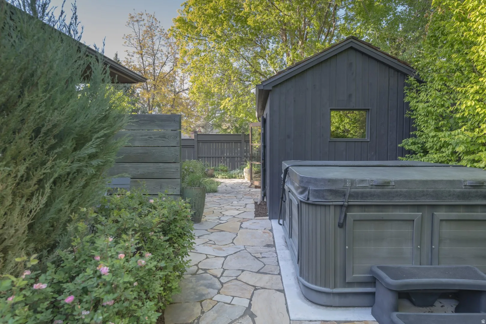 Flagstone pathway, wood privacy fencing, mature landscaping, and a dark-clad outbuilding