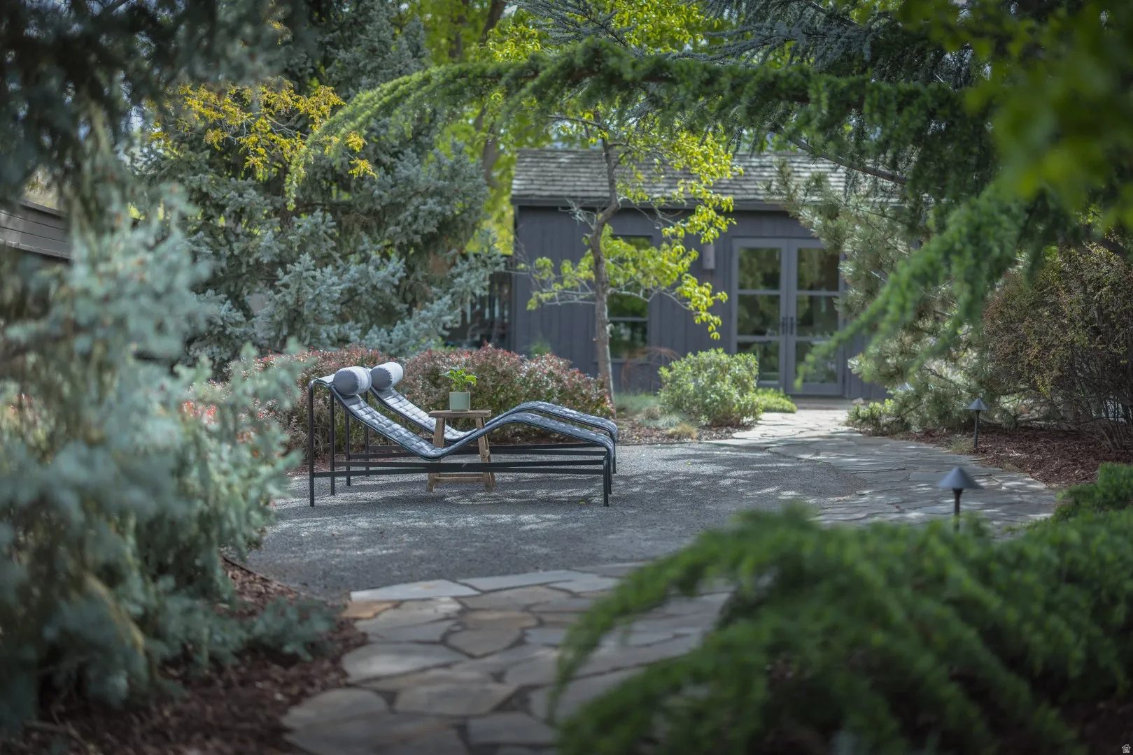 Landscaped grounds with a flagstone path, gravel patio, perimeter lighting, and mature trees
