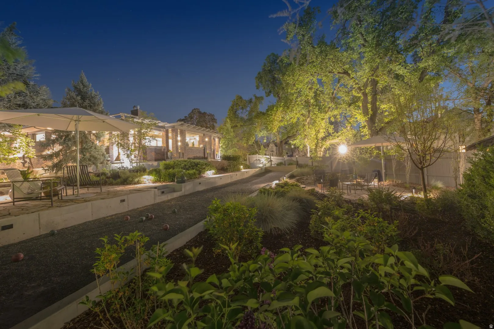 Expansive outdoor living area featuring a bocce ball court, tiered landscaping, and mature trees