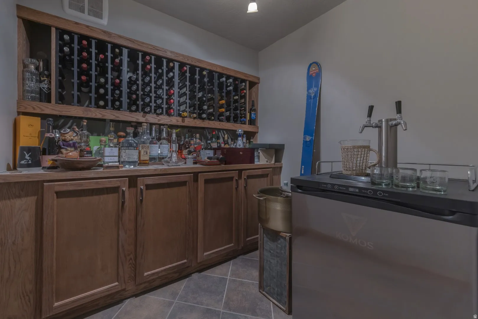 Built-in wine storage, extensive cabinetry with wood-finish doors, countertop space, tiled flooring, and a beverage refrigerator with a double tap